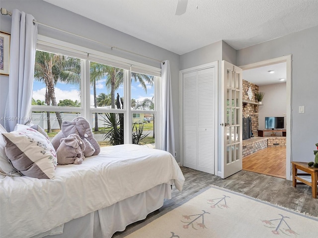 bedroom featuring a closet, a brick fireplace, ceiling fan, a textured ceiling, and light wood-type flooring