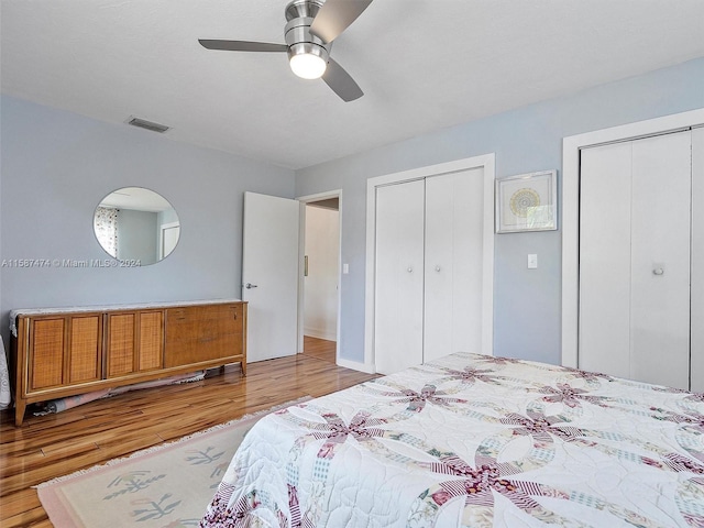 bedroom featuring ceiling fan, light hardwood / wood-style floors, and two closets