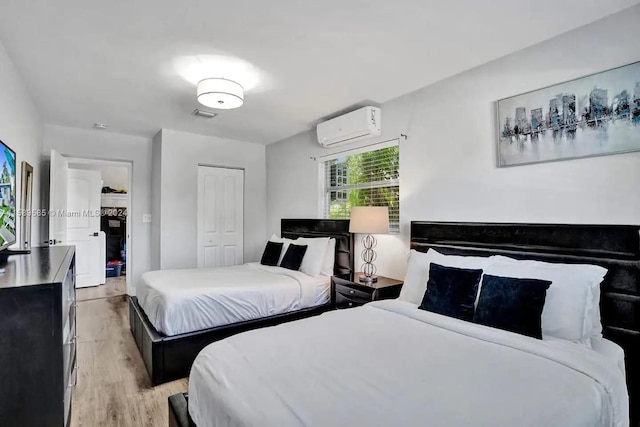 bedroom with light hardwood / wood-style floors, an AC wall unit, and a closet