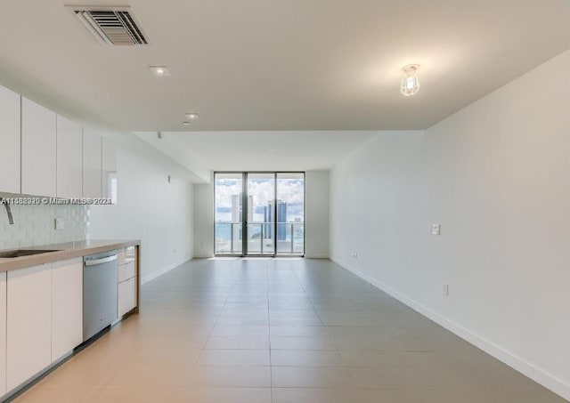 interior space featuring expansive windows, tasteful backsplash, stainless steel dishwasher, sink, and white cabinets