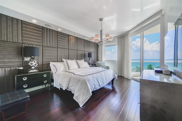 bedroom featuring dark wood-type flooring, access to outside, a notable chandelier, and a water view