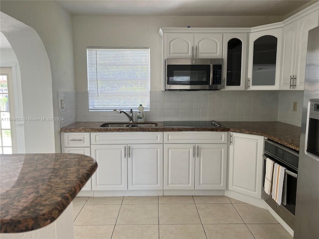 kitchen with appliances with stainless steel finishes, white cabinets, sink, tasteful backsplash, and light tile flooring