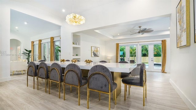 dining area with french doors, a raised ceiling, built in features, light hardwood / wood-style flooring, and ceiling fan with notable chandelier