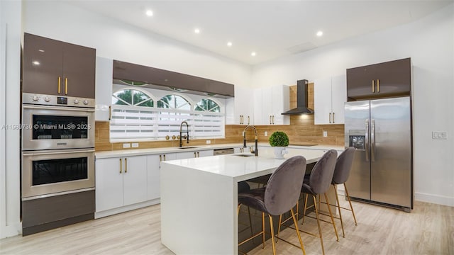 kitchen with a center island with sink, sink, a breakfast bar area, wall chimney exhaust hood, and stainless steel appliances