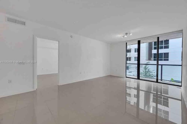 tiled spare room featuring track lighting and a wall of windows