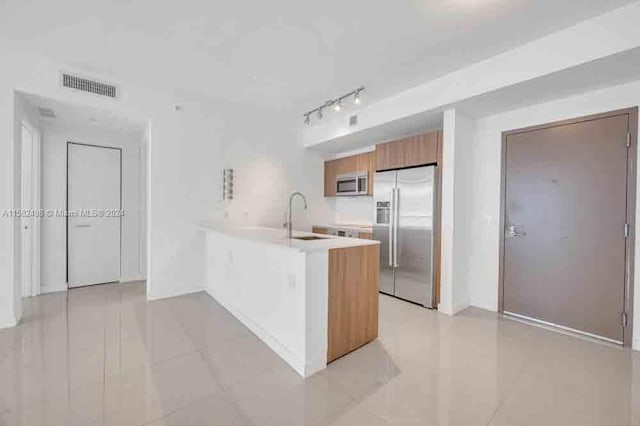 kitchen with stainless steel appliances, kitchen peninsula, rail lighting, sink, and light tile floors