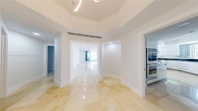 hallway with a raised ceiling and light tile floors