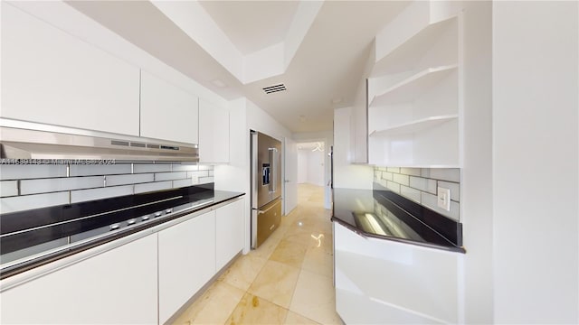 kitchen with wall chimney range hood, high end fridge, backsplash, white cabinets, and light tile floors