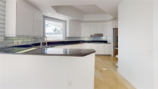 kitchen featuring white cabinetry, tasteful backsplash, a tray ceiling, and kitchen peninsula