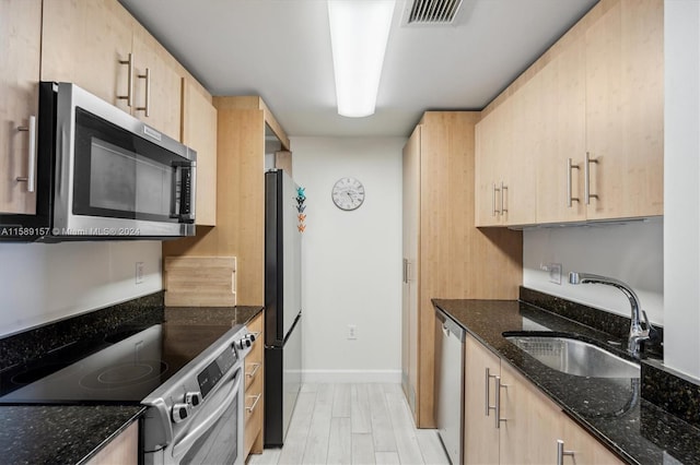 kitchen featuring light brown cabinets, sink, light hardwood / wood-style flooring, dark stone countertops, and appliances with stainless steel finishes