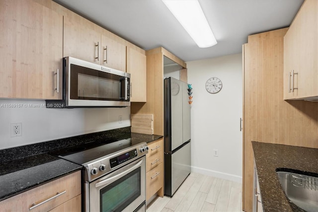 kitchen featuring dark stone countertops, light brown cabinetry, light wood-type flooring, and appliances with stainless steel finishes