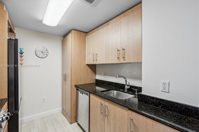 kitchen with dark stone countertops, dishwasher, sink, and light brown cabinetry