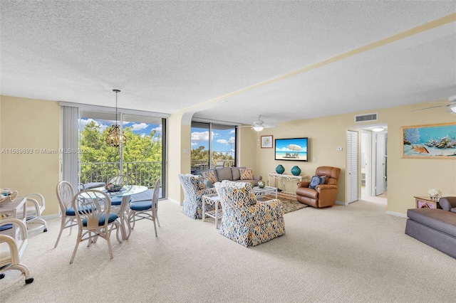 carpeted living room featuring a textured ceiling, a wall of windows, and ceiling fan with notable chandelier