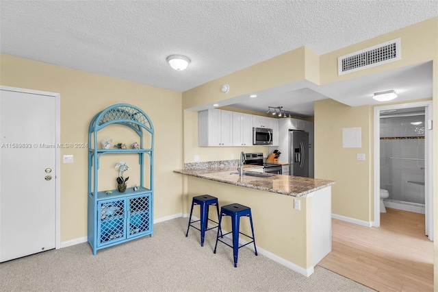 kitchen featuring light wood-type flooring, appliances with stainless steel finishes, white cabinets, a breakfast bar area, and kitchen peninsula