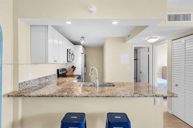 kitchen with light stone countertops, light wood-type flooring, appliances with stainless steel finishes, kitchen peninsula, and sink