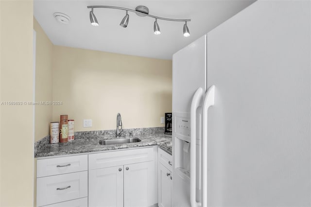 kitchen with white cabinetry, light stone countertops, rail lighting, sink, and white refrigerator with ice dispenser