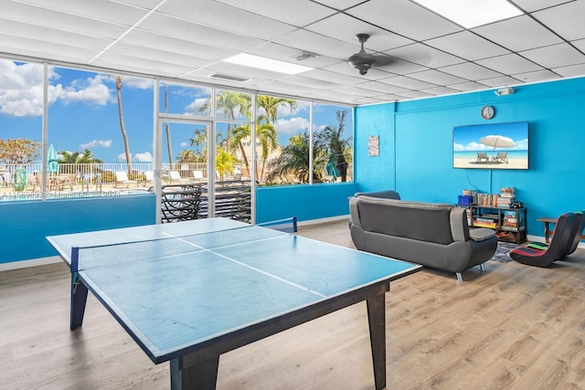 playroom featuring hardwood / wood-style floors, expansive windows, ceiling fan, and a drop ceiling