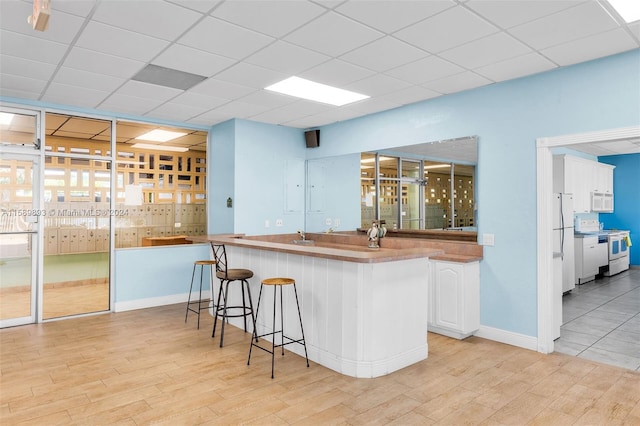 kitchen with white cabinetry, white appliances, a kitchen bar, and a drop ceiling