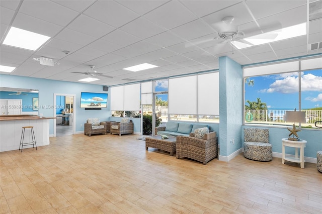 living room featuring ceiling fan, a healthy amount of sunlight, light hardwood / wood-style floors, and a drop ceiling