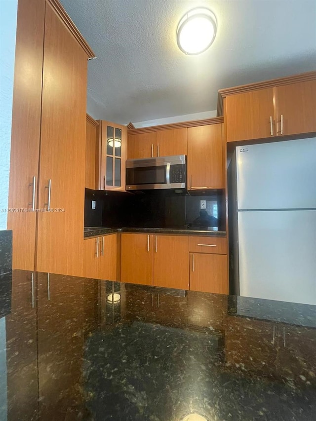 kitchen featuring dark stone counters, white fridge, tasteful backsplash, and a textured ceiling