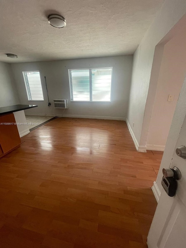 unfurnished room featuring a textured ceiling, a wall mounted air conditioner, and hardwood / wood-style floors