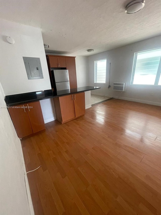 kitchen with a wall unit AC, kitchen peninsula, hardwood / wood-style floors, and white fridge