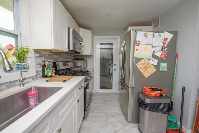 kitchen with sink, independent washer and dryer, appliances with stainless steel finishes, tasteful backsplash, and white cabinetry