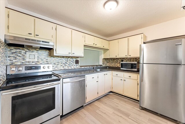 kitchen with light hardwood / wood-style floors, stainless steel appliances, tasteful backsplash, sink, and a textured ceiling