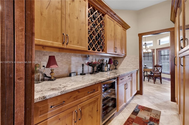 bar with decorative backsplash, light stone countertops, beverage cooler, and an inviting chandelier