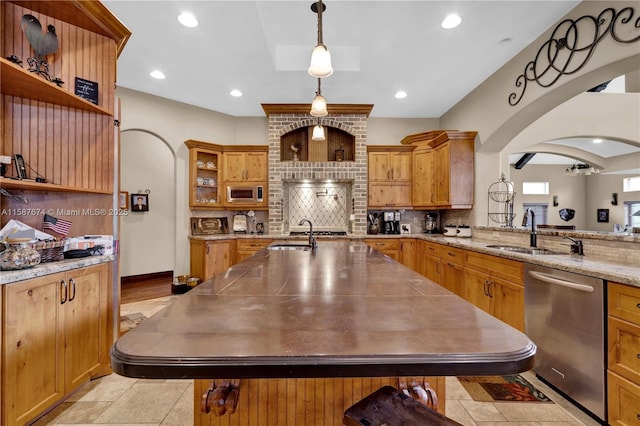 kitchen with light stone countertops, appliances with stainless steel finishes, decorative light fixtures, sink, and backsplash