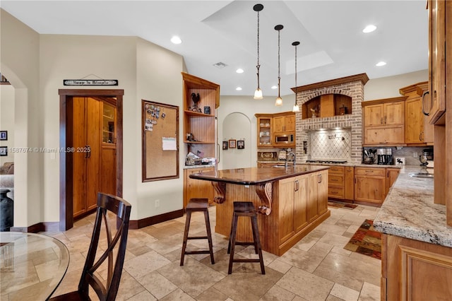 kitchen with pendant lighting, appliances with stainless steel finishes, tasteful backsplash, a kitchen island with sink, and a breakfast bar