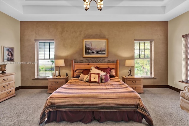 bedroom featuring light colored carpet, multiple windows, a tray ceiling, and a chandelier