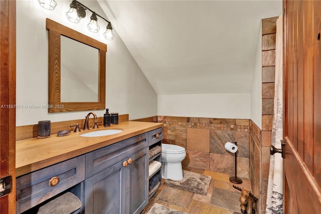 bathroom with toilet, vanity, and lofted ceiling