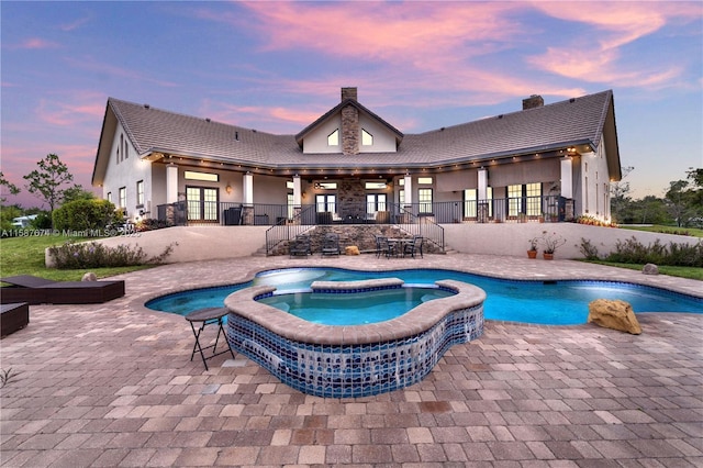 pool at dusk featuring an in ground hot tub and a patio area