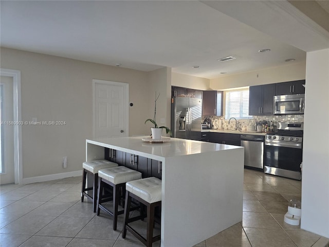 kitchen featuring tasteful backsplash, light tile flooring, a kitchen island, a breakfast bar area, and appliances with stainless steel finishes