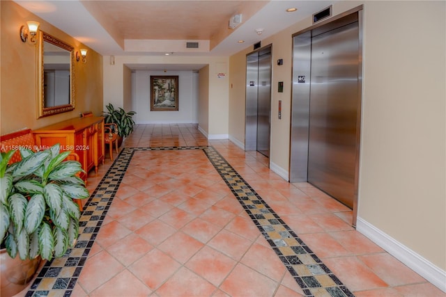 corridor with light tile patterned flooring, a raised ceiling, and elevator