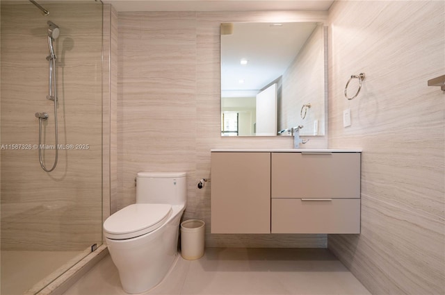 bathroom with tile walls, toilet, vanity, tiled shower, and tile patterned floors