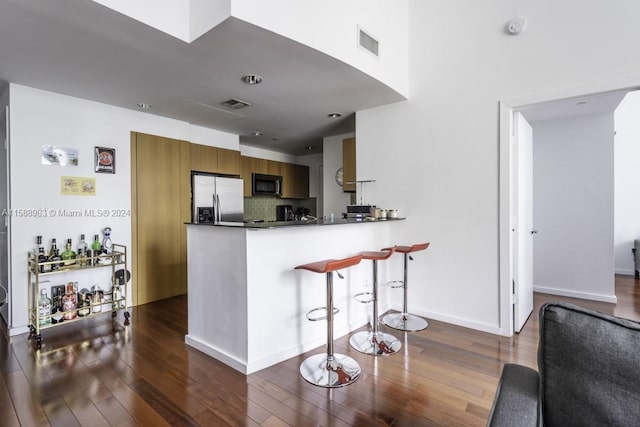 kitchen featuring kitchen peninsula, stainless steel fridge, dark hardwood / wood-style flooring, backsplash, and a breakfast bar