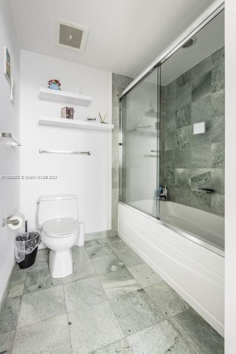 bathroom featuring combined bath / shower with glass door, toilet, and tile floors