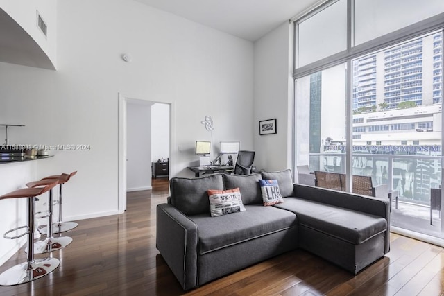 living room with a high ceiling, dark wood-type flooring, and a wall of windows