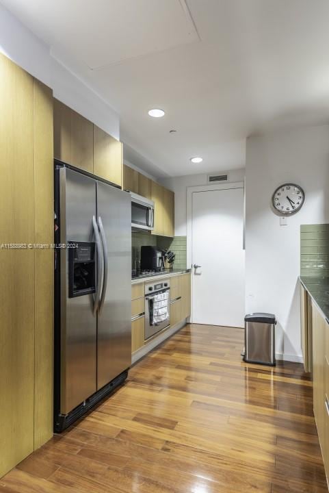 kitchen with stainless steel appliances, hardwood / wood-style flooring, and backsplash