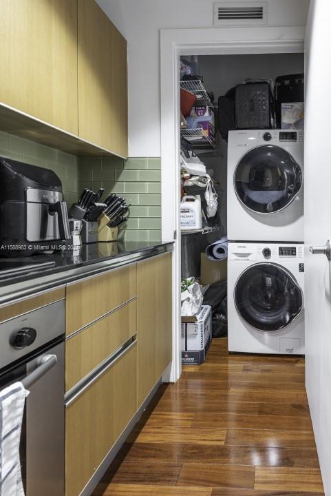 clothes washing area featuring dark wood-type flooring and stacked washer / drying machine