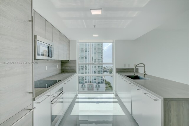 kitchen with black electric stovetop, expansive windows, wall oven, sink, and tile patterned flooring