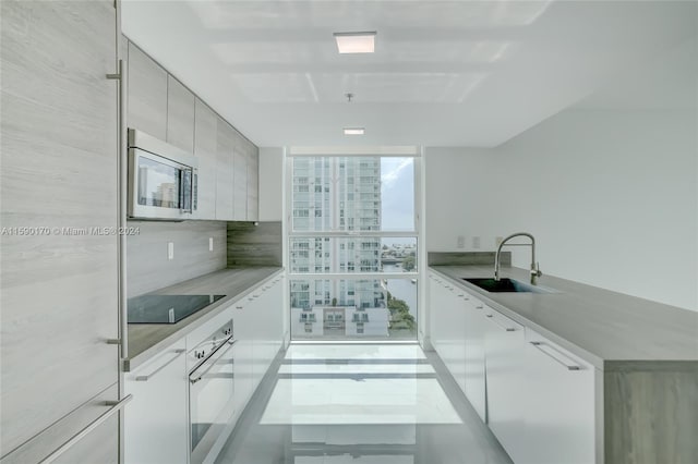 kitchen with sink, oven, backsplash, expansive windows, and black electric stovetop