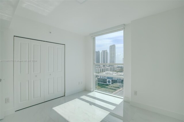 unfurnished bedroom featuring multiple windows, tile patterned flooring, a closet, and a wall of windows