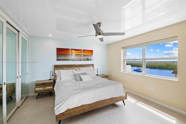 bedroom with a water view, ceiling fan, and light tile floors