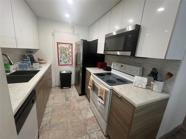 kitchen with white appliances, backsplash, white cabinetry, and sink