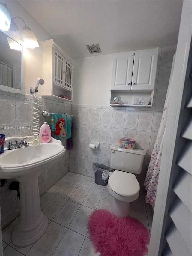 bathroom featuring toilet, tile patterned floors, and tile walls