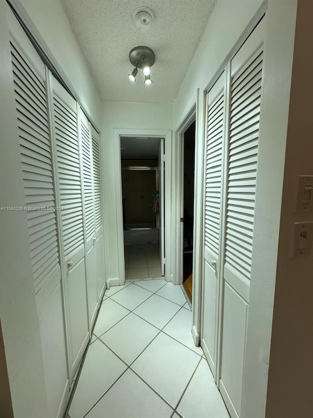 hallway with a textured ceiling and light tile floors