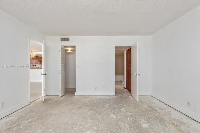 unfurnished bedroom with a chandelier, a closet, a textured ceiling, and ensuite bath